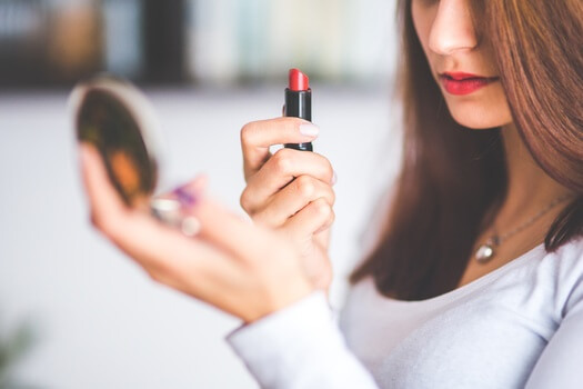 woman holding up a compact mirror and putting on red lipstick