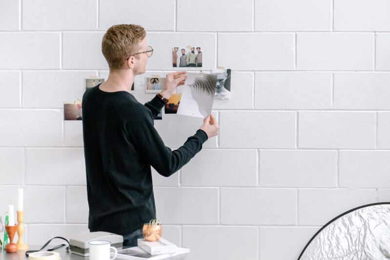 Man placing photos on white wall.