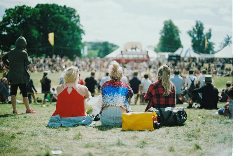 Three girlfriends sitting on field at a music festival
