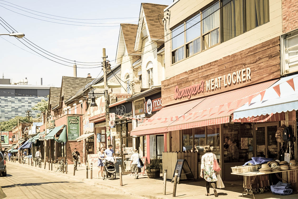 Pedestrians walk beside colourful shops in the hip Kensington Market neighbourhood of central Toronto, Ontario.