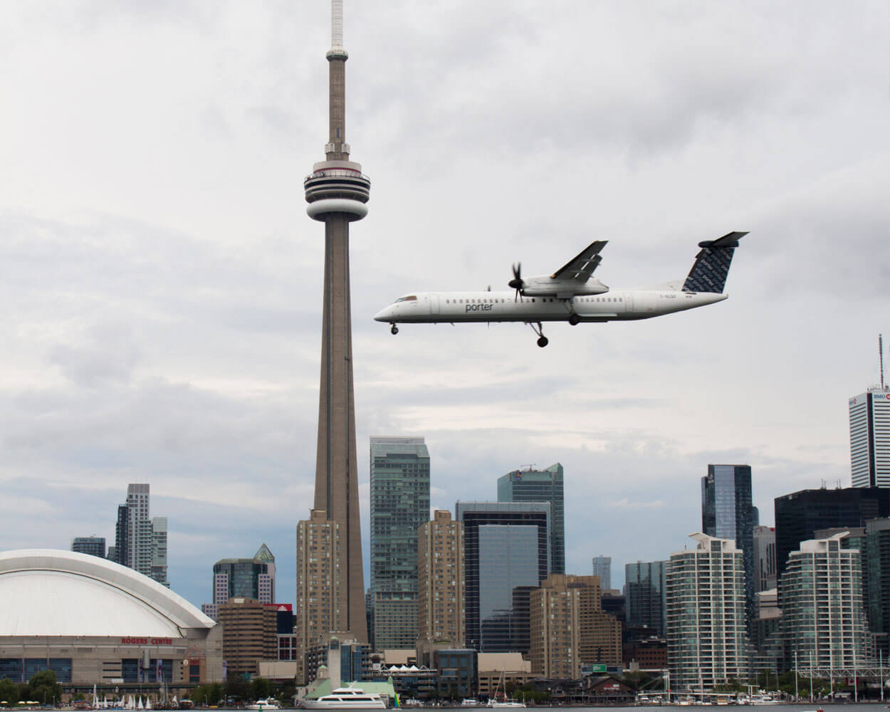 an airplane passes in front of the CN Tower and Toronto skyline, landing at the Toronto Island Airport