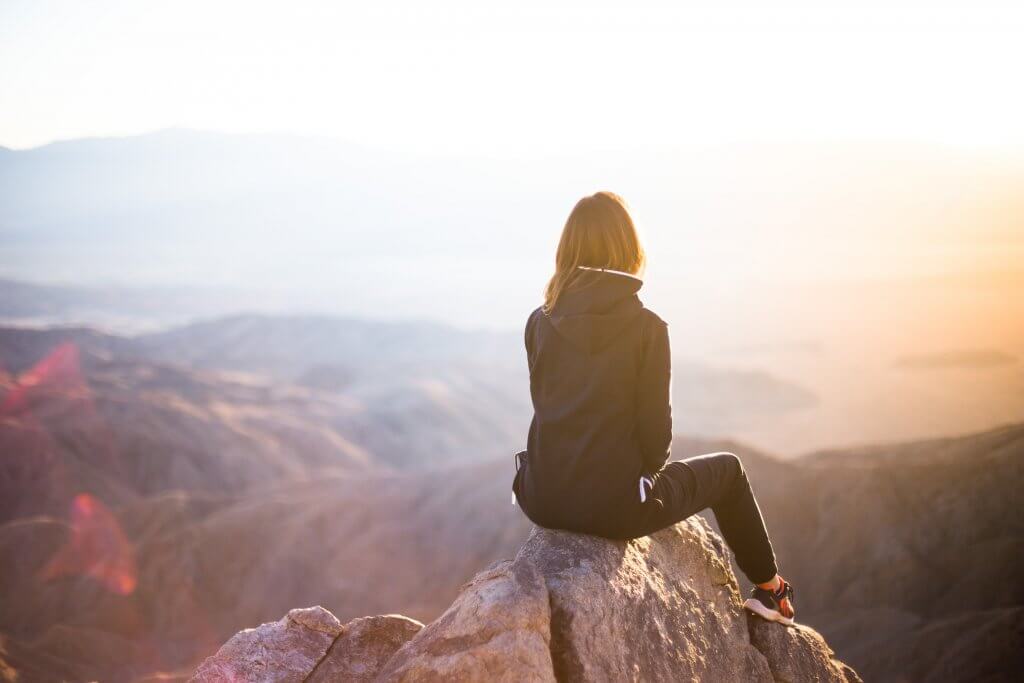 Athletic girl sitting on top of a mountain overlooking several mountains against a clear sky 