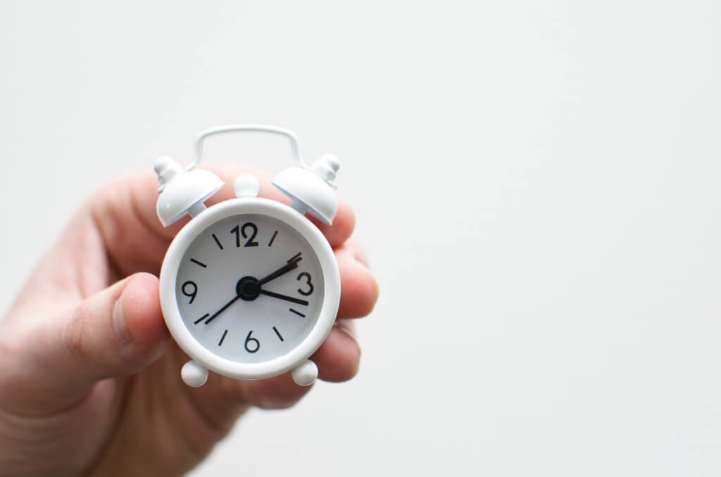 Small white clock being held up by a hand