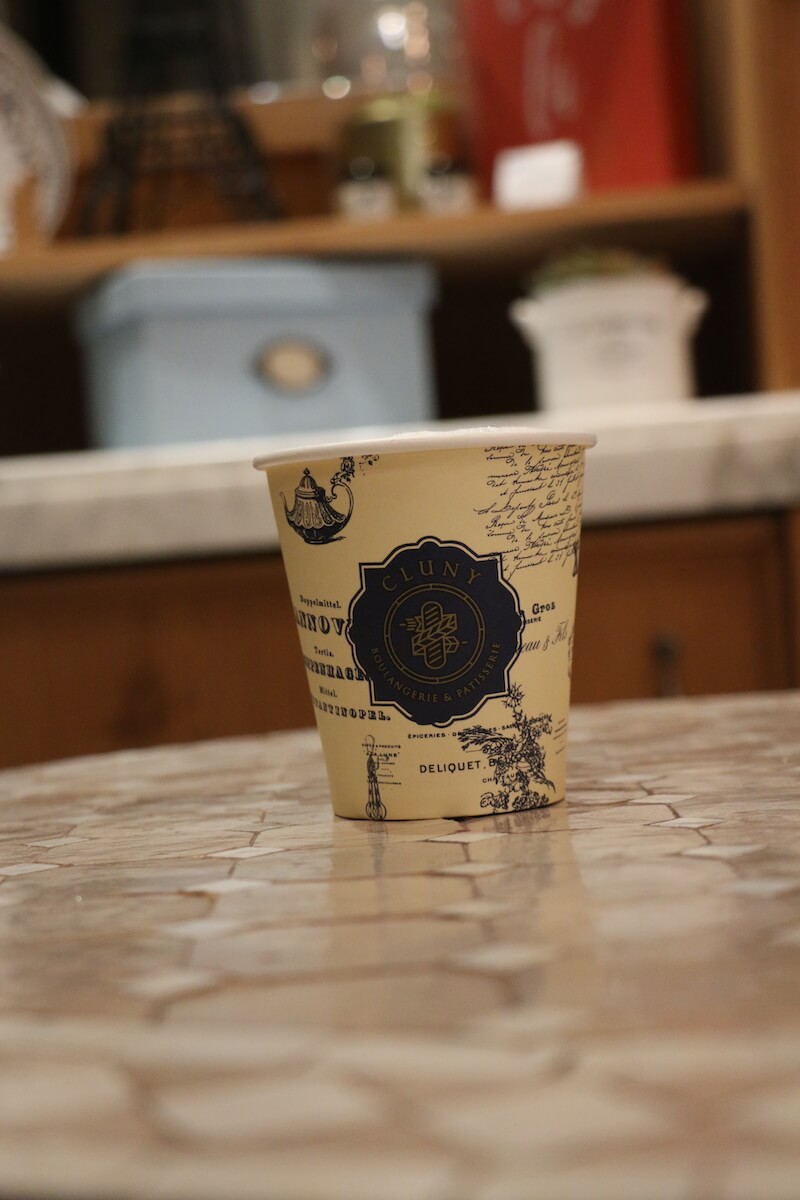 Takeout coffee cup readinf "Cluny Boulangerie and Patisserie" on marble table