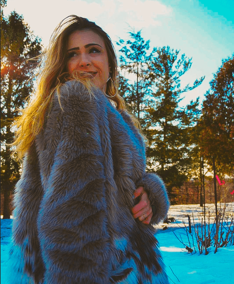 girl in fur coat in woods, smiling and looking over shoulder