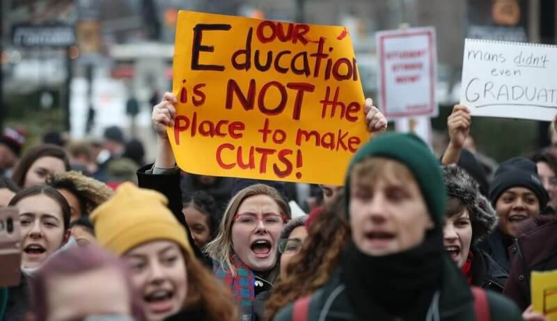 Girl protesting and holding sign that reads "Our education is not the place to make cuts"
