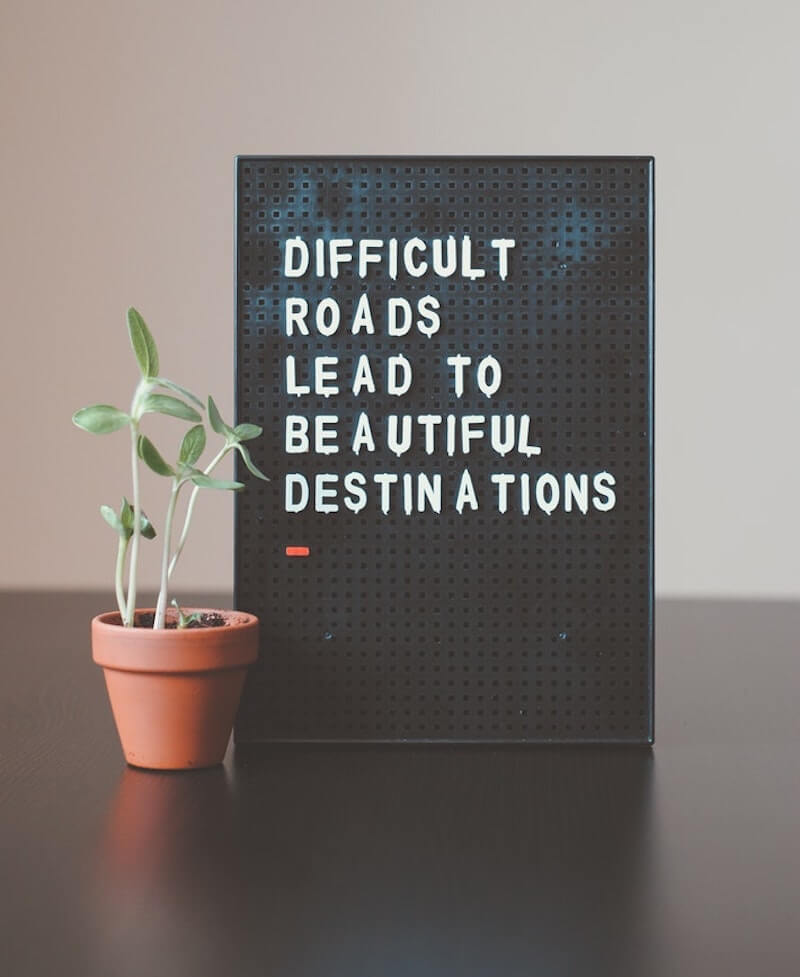 Sign reading "difficult roads lead to beautiful destinations" next to a plant pot