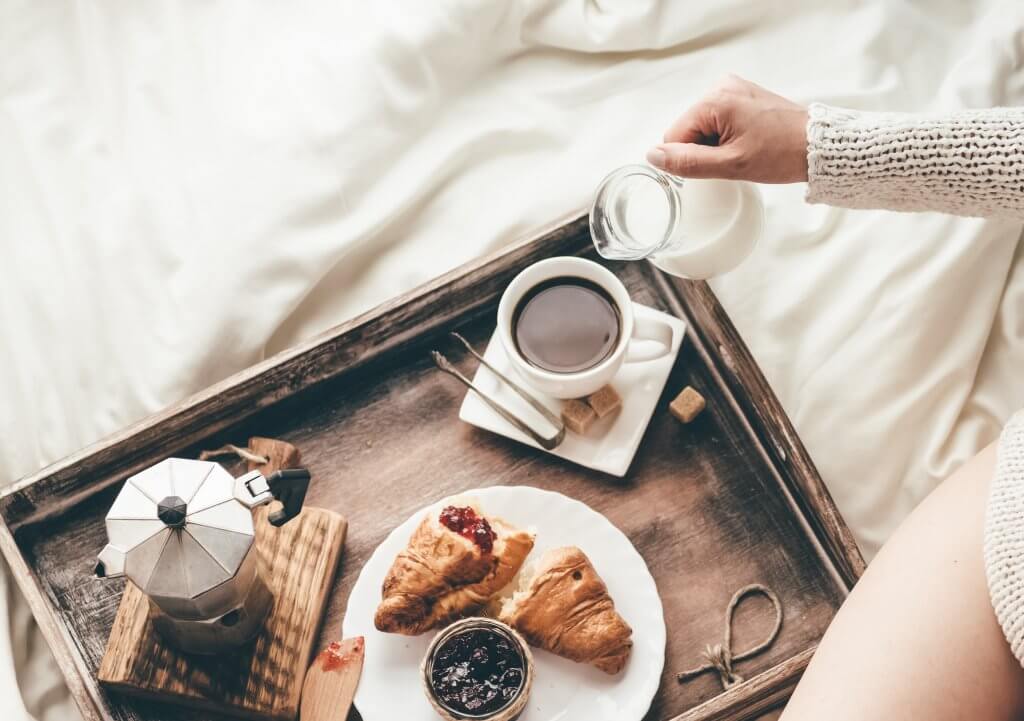 breakfast in bed on a tray, women pouring milk into coffee,