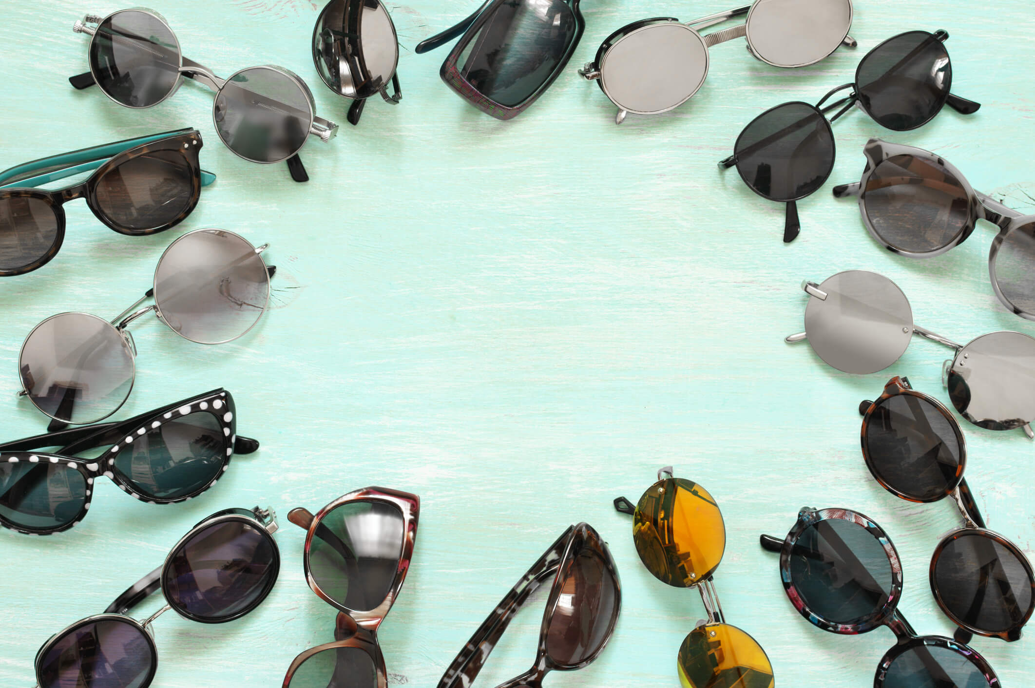 Variety of sunglasses lying as frame on mint colored wooden background. Top view point, flat lay.