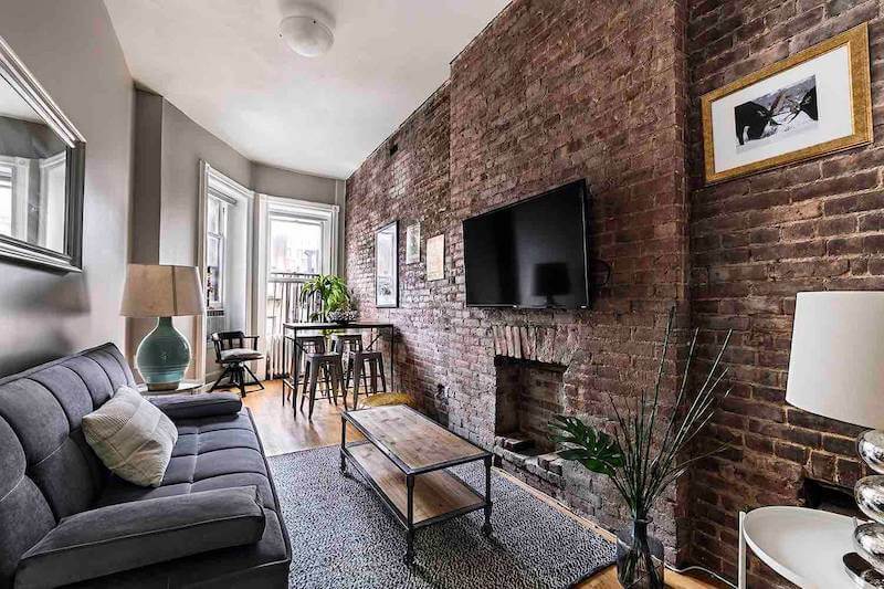 View of apartment living room with brick walls, couch, and TV