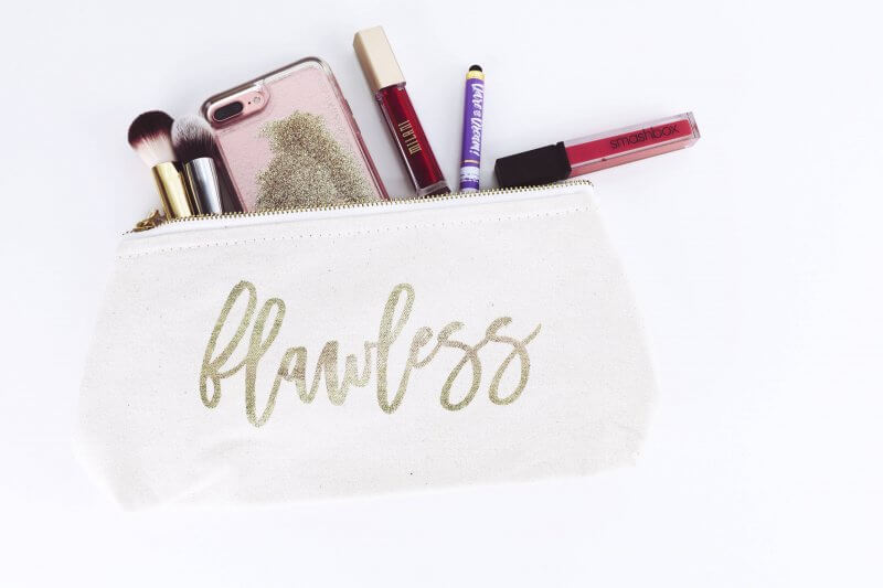 A makeup bag reading "flawless" with brushes, lipsticks and an iphone spilling out