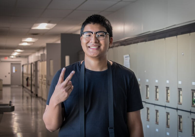Boy holding up peace sign, wearing black shirt in front of lockers