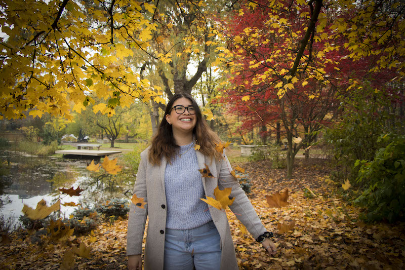 girl with glasses smiling in front of colourful trees