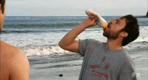 Guy on beach squeezing sunscreen into mouth
