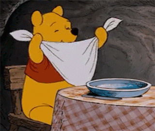Winnie the Pooh ties a napkin around his neck and licks his lips in excitement for his meal.
