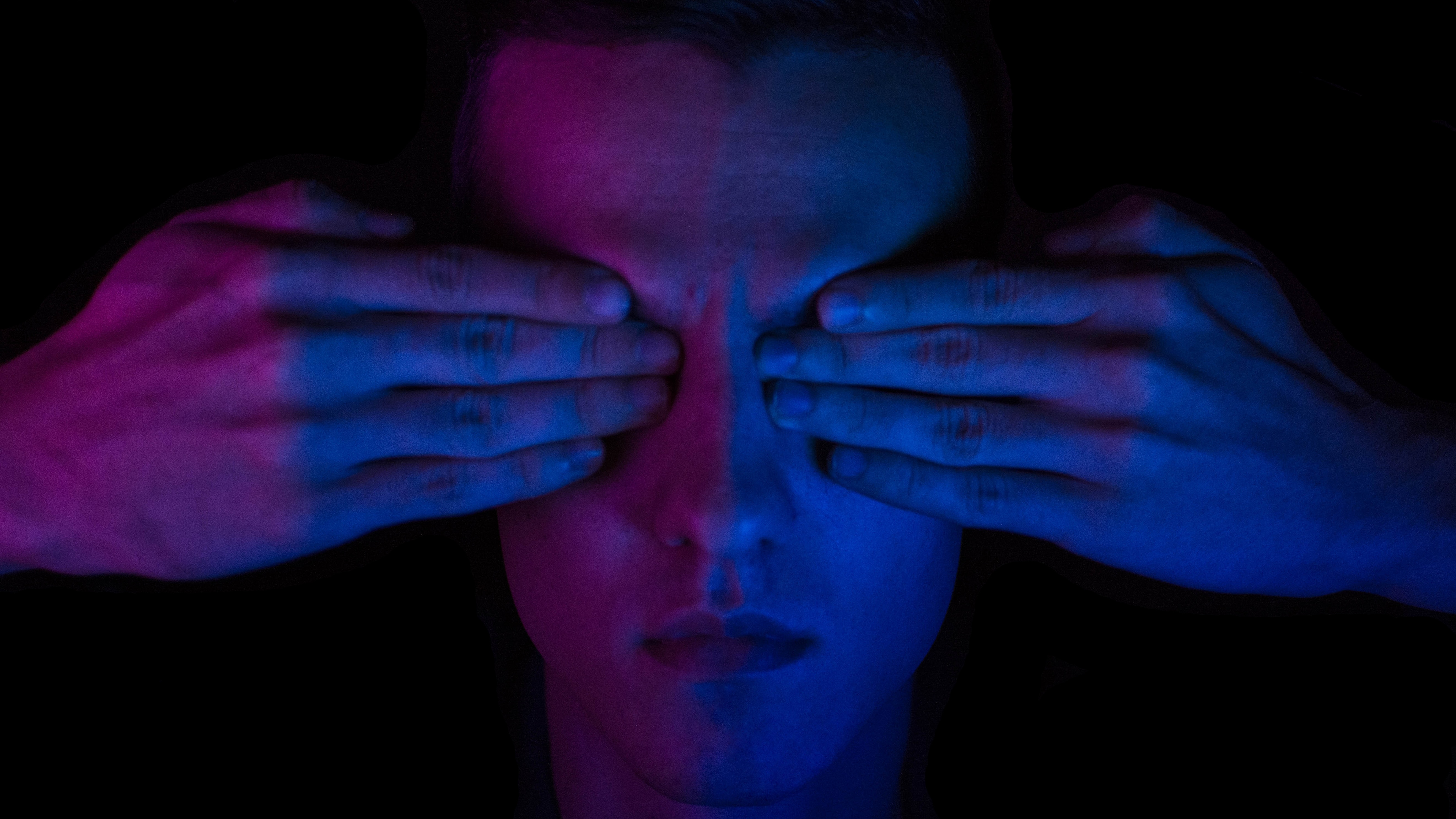 close-up of a man's face with his eyes covered illuminated with blue and purple lights.