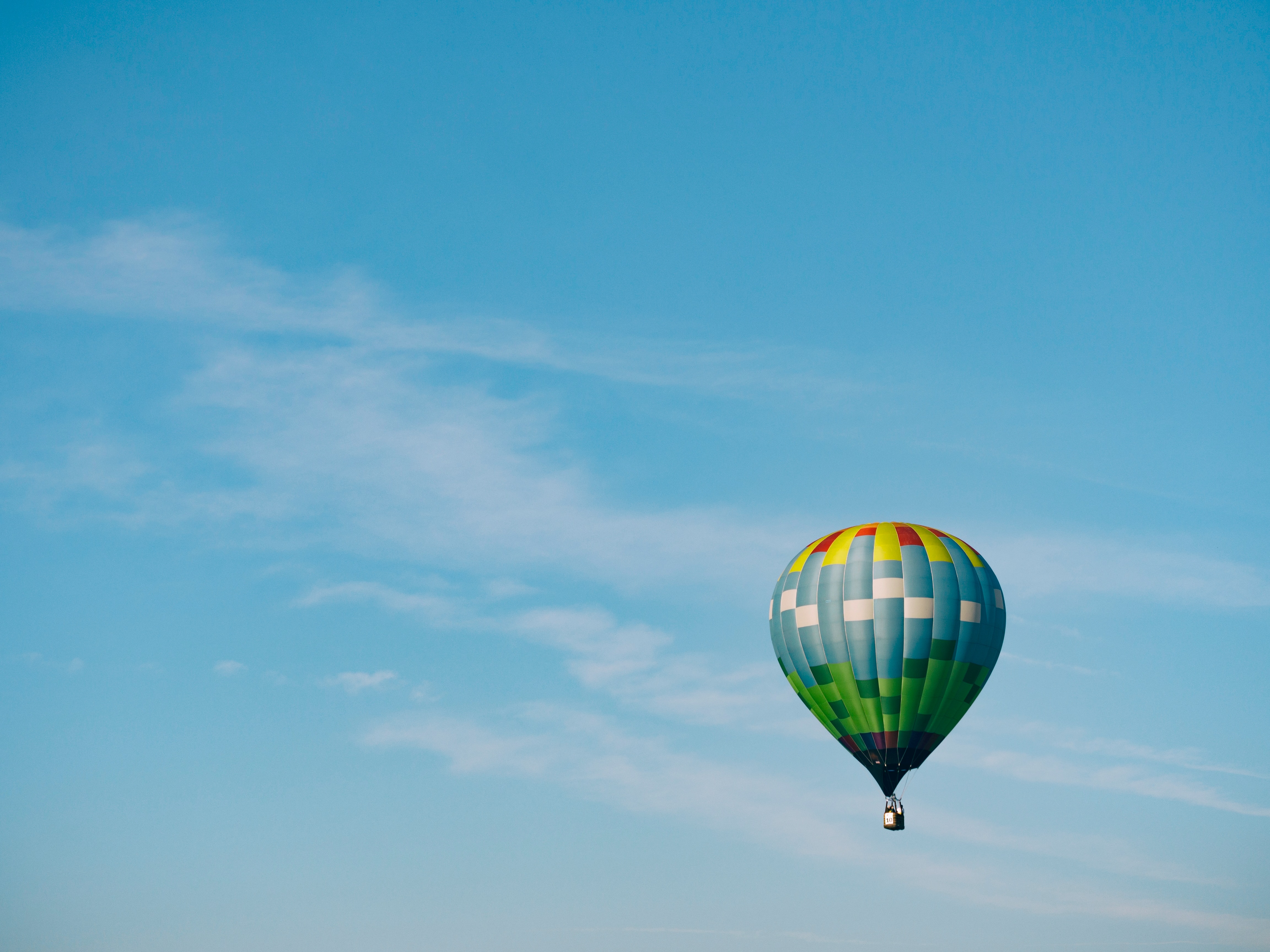 a red and green hot air balloon floats into a clear blue sky.