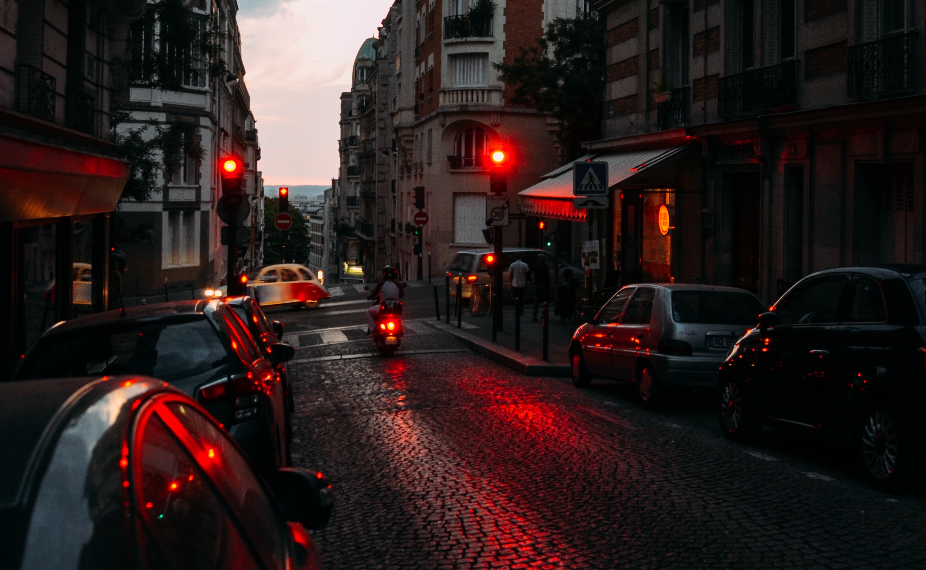 red traffic lights illuminate a dark cobblestone street.