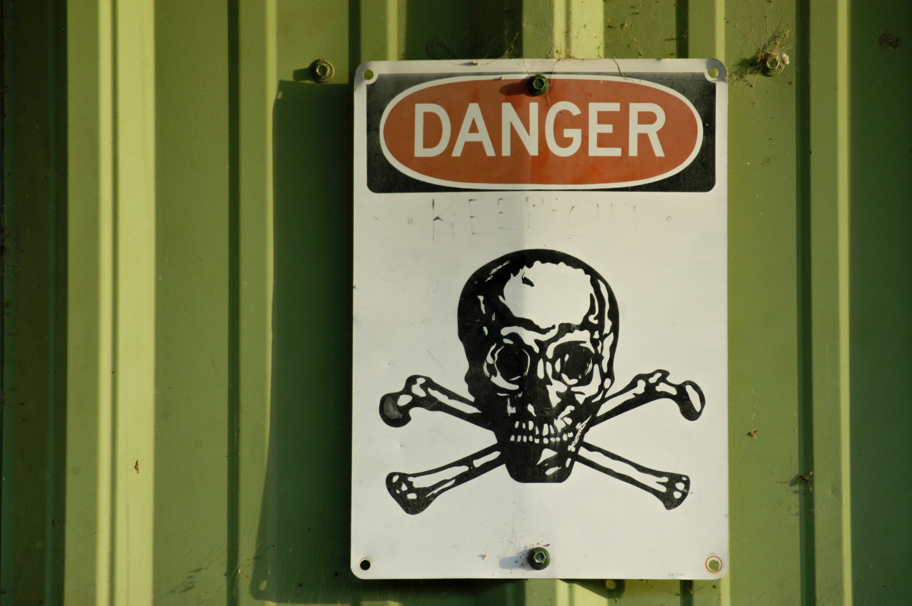 a danger sign featuring a skull and crossbones posted on a green wall