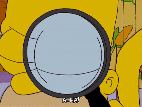 Homer Simpson from, "The Simpsons," holds a magnifying glass up to his eye and says, "A-ha!"