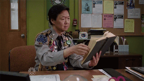 Ben Chang from the TV show, "Community," overdramatically flips a page in a book, looks into the camera, and smiles.