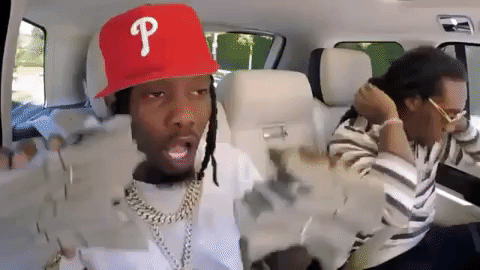 Gif of Offset from the rap group Migos dancing while holding two large stacks of bills.