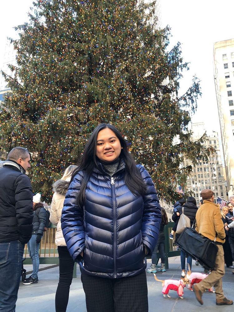 Third year University of Guelph-Humber media studies media business student Kim Leon stands outside in front of a Christmas tree and smiles.