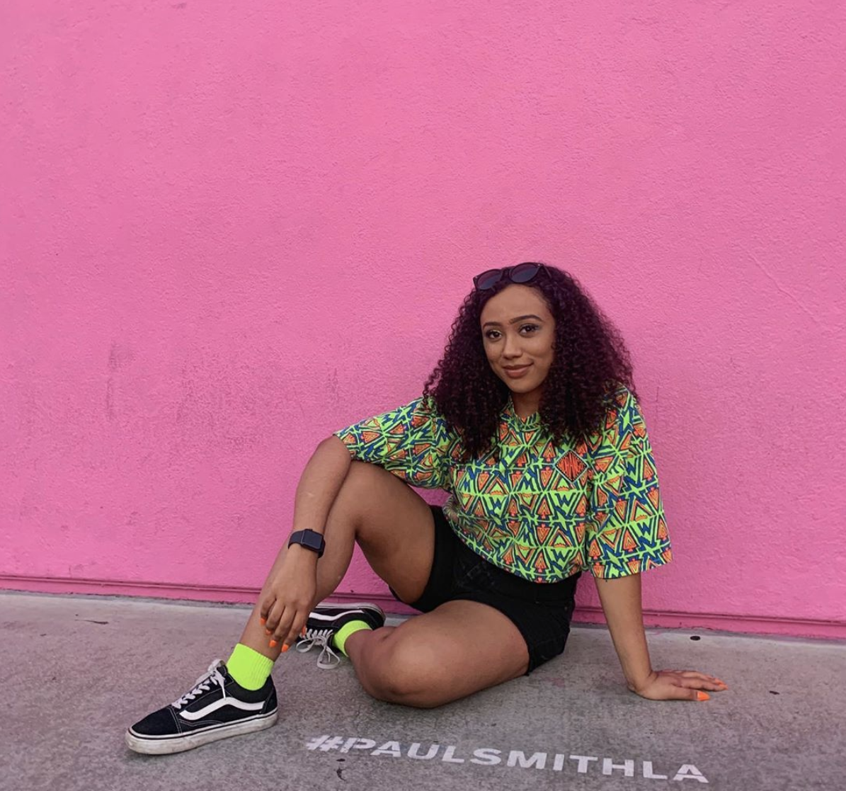 Fourth year media studies public relations and journalism student Danya Elsayed sits in front of a pink wall in Los Angeles and smiles.