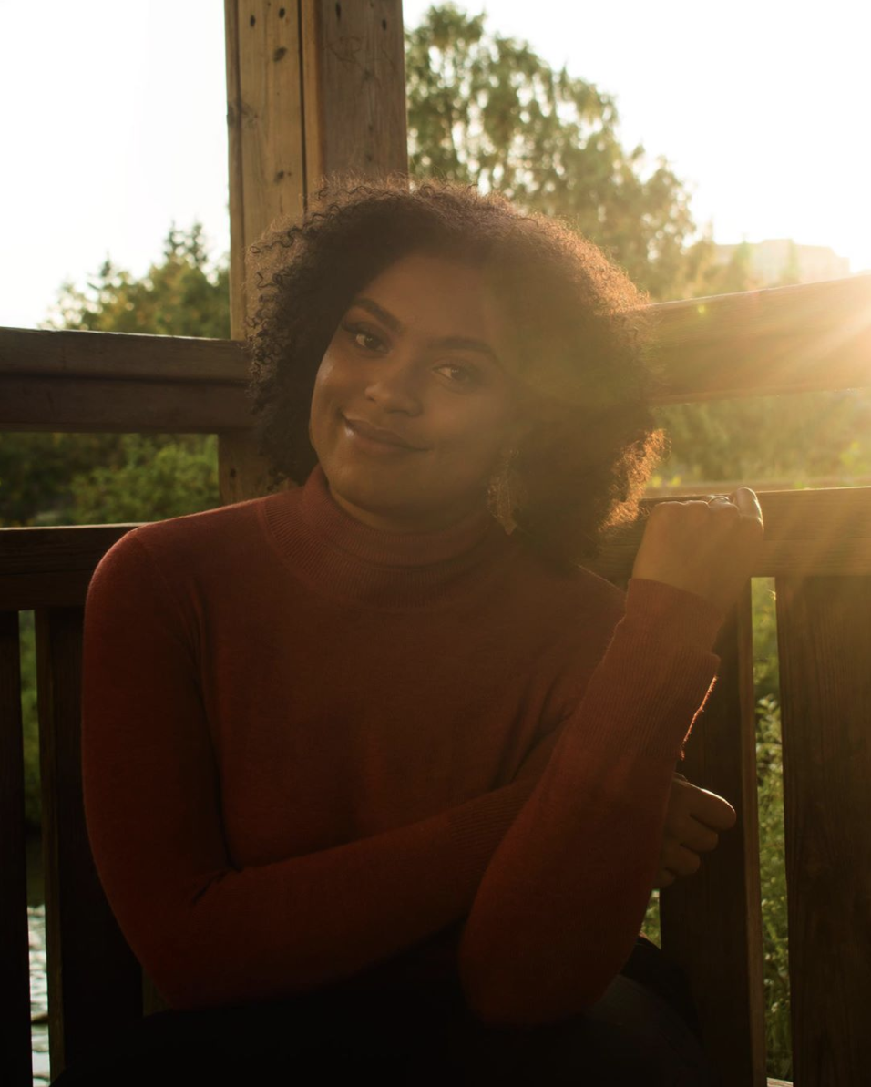 Second year University of Guelph-Humber psychology student Casiah Cagan sits in the sun in a red turtleneck sweater and smiles.