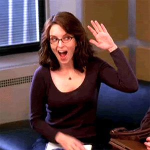 Tina Fey as Liz Lemon in "30 Rock" high fives herself and then points forward while smiling.