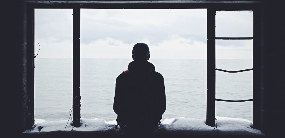 person sitting alone in front of an open window overlooking water