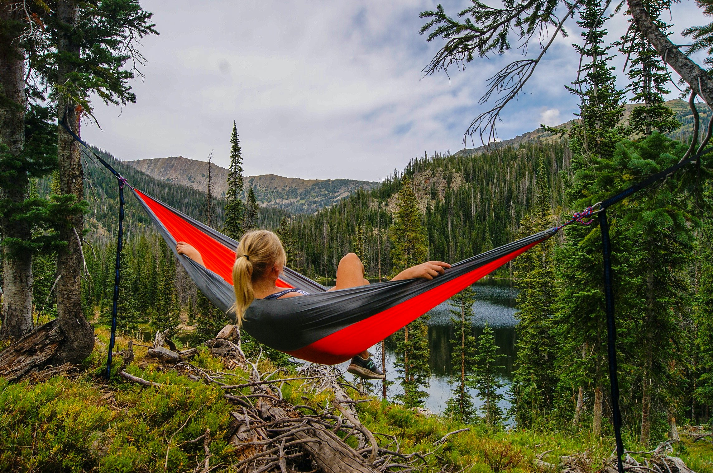 A girl sits in a hammock overlooking a lake