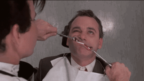 aerial view of a man laying in a dentist's chair as the dentist manipulates his mouth into goofy expressions with metal tools.