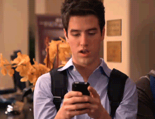 Logan Henderson as Logan Mitchell on Nickelodeon's "Big Time Rush" (2009-2013) points energetically at his smartphone before replying to a text.