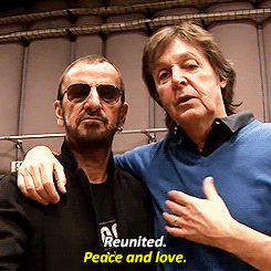 Paul McCartney and Ringo Starr of The Beatles have their arms around one another and form peace signs with their hands. Starr says, "Reunited," and McCartney says, "Peace and love."