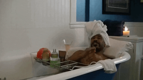 Scene from "Love & Hip Hop" depicting a man with a towel wrapped around his head sitting in a bubble nath with a class of champagne and a candle.