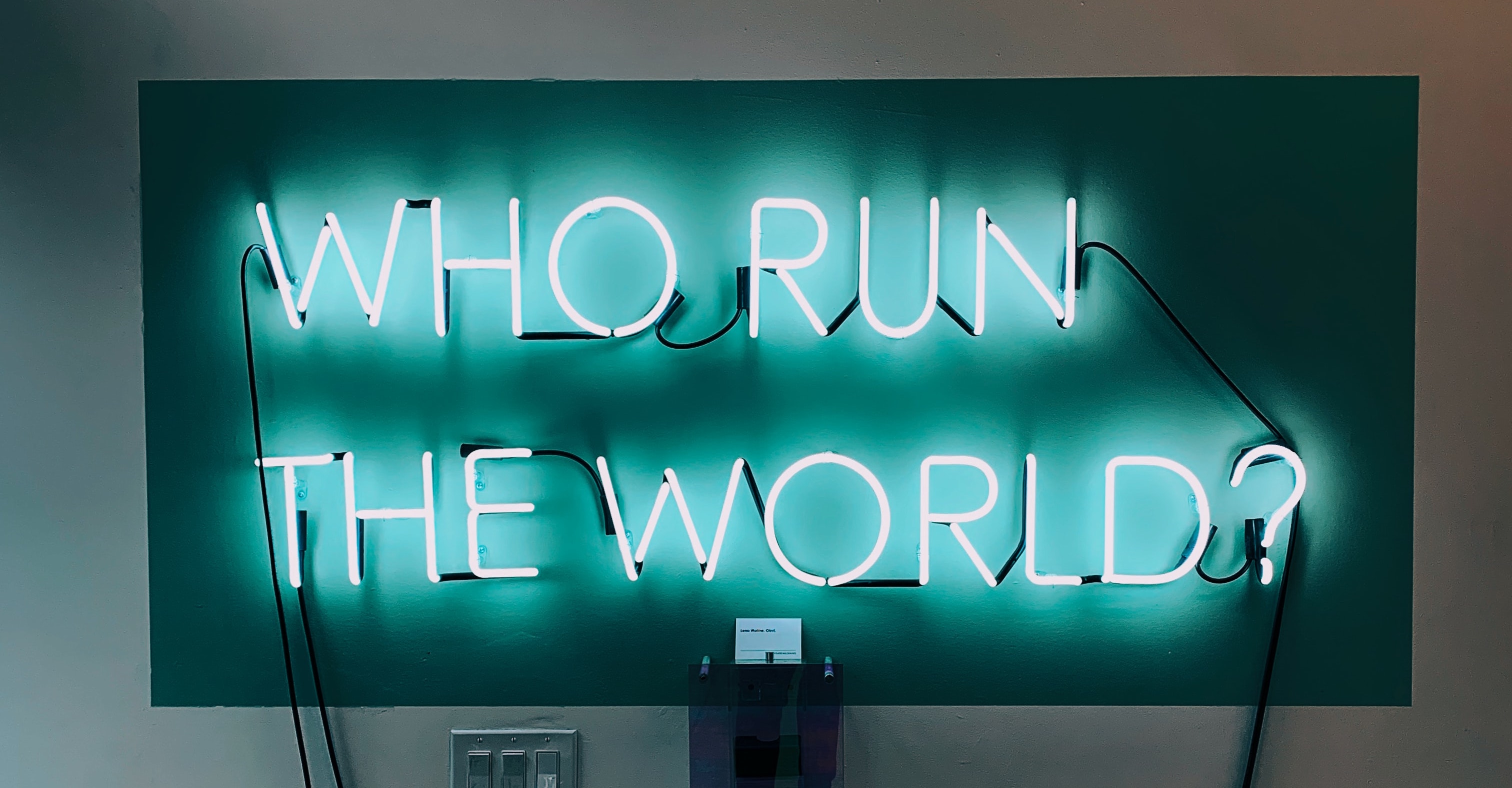 A neon sign featuring the Beyonce lyric, "Who run the world?" in blue block letters.