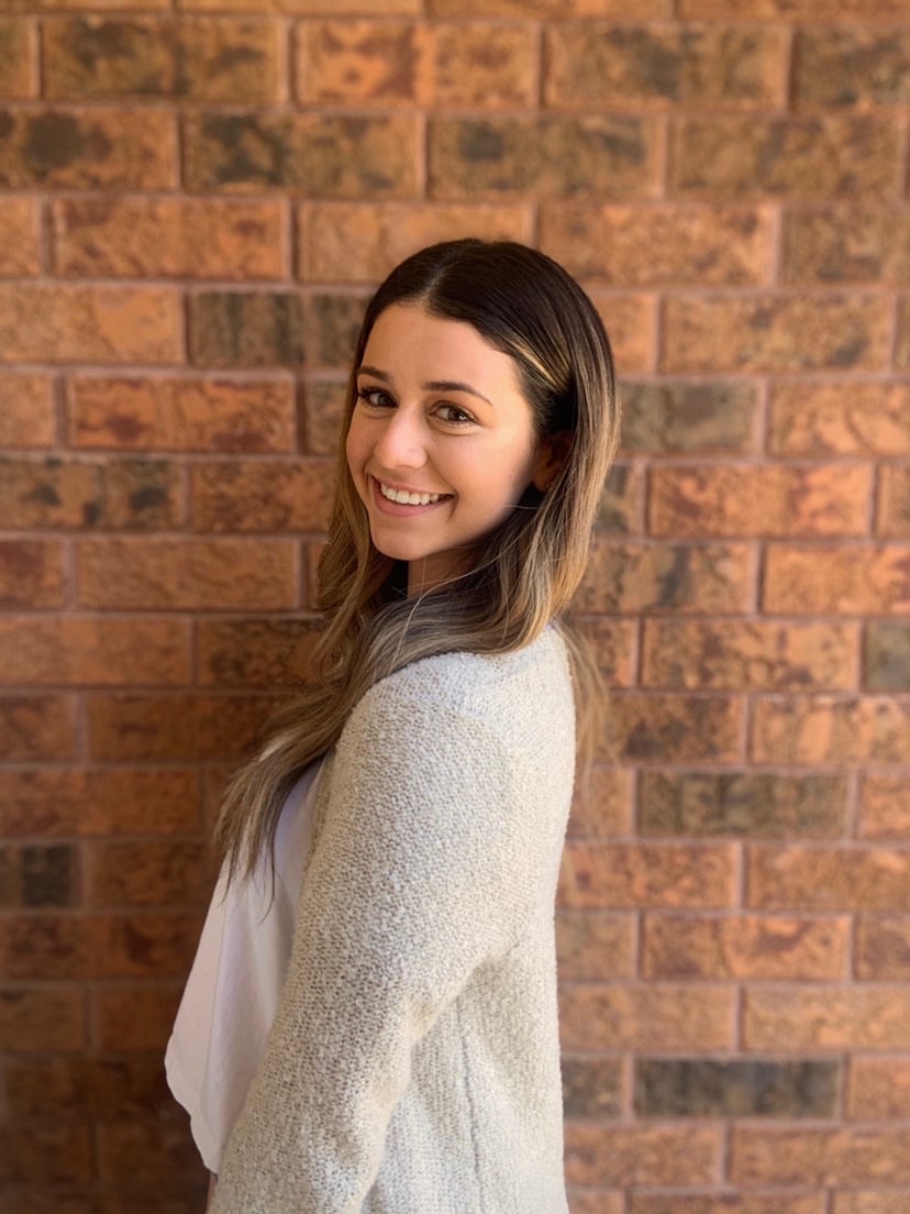 Julia Ciampa, a University of Guelph-Humber Justice Studies student, stands facing left and looking at the camera over her left shoulder. She is smiling and wearing a light grey cardigan.