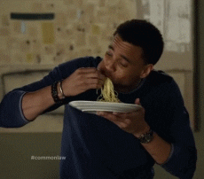 A man wearing a navy blue t-shirt messily eats spaghetti with his hands.