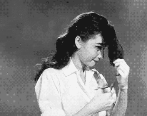 Greyscale gif of Audrey Hepburn playfully swatting at her chin-length bangs. She wears a white blouse.