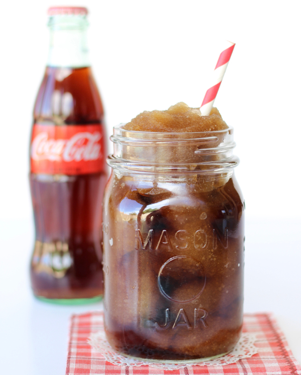 A homemade Coke slushie in a mason jar with a red and white straw.