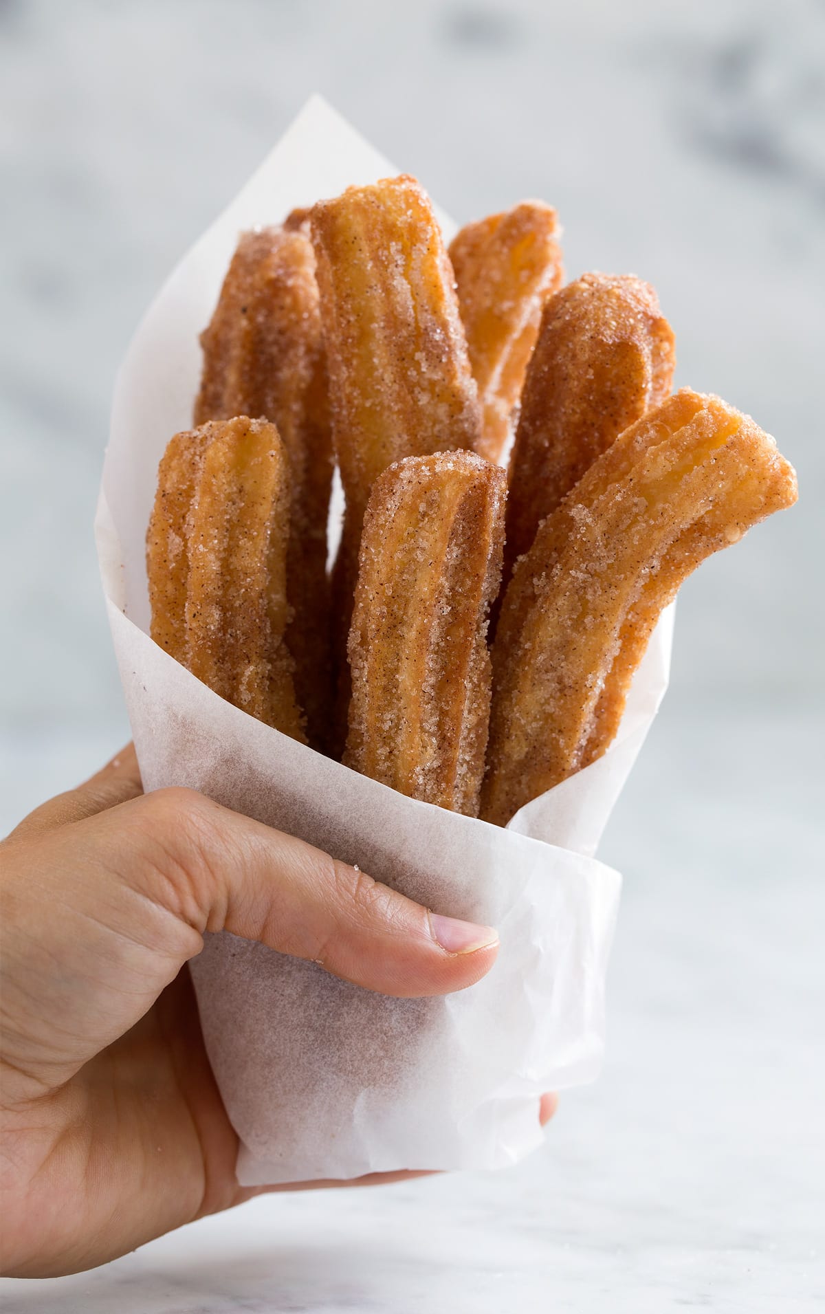 a person holding a bouquet of churros in white paper wrapping.