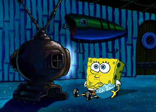 Spongebob Squarepants sits in front of a TV in a dark room eating popcorn.