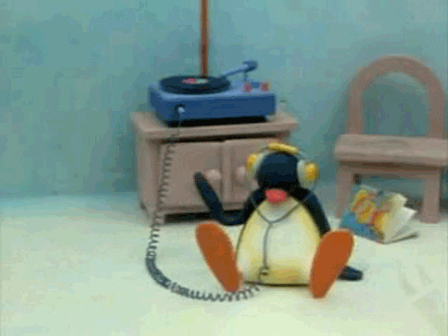 Pingu the penguin sits on the floor wearing headphones while joyfully tapping the floor next to him.