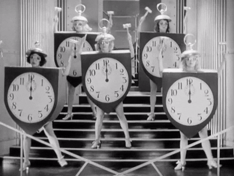 Women in black and white dancing dressed up as clocks banging their heads with wooden hammered