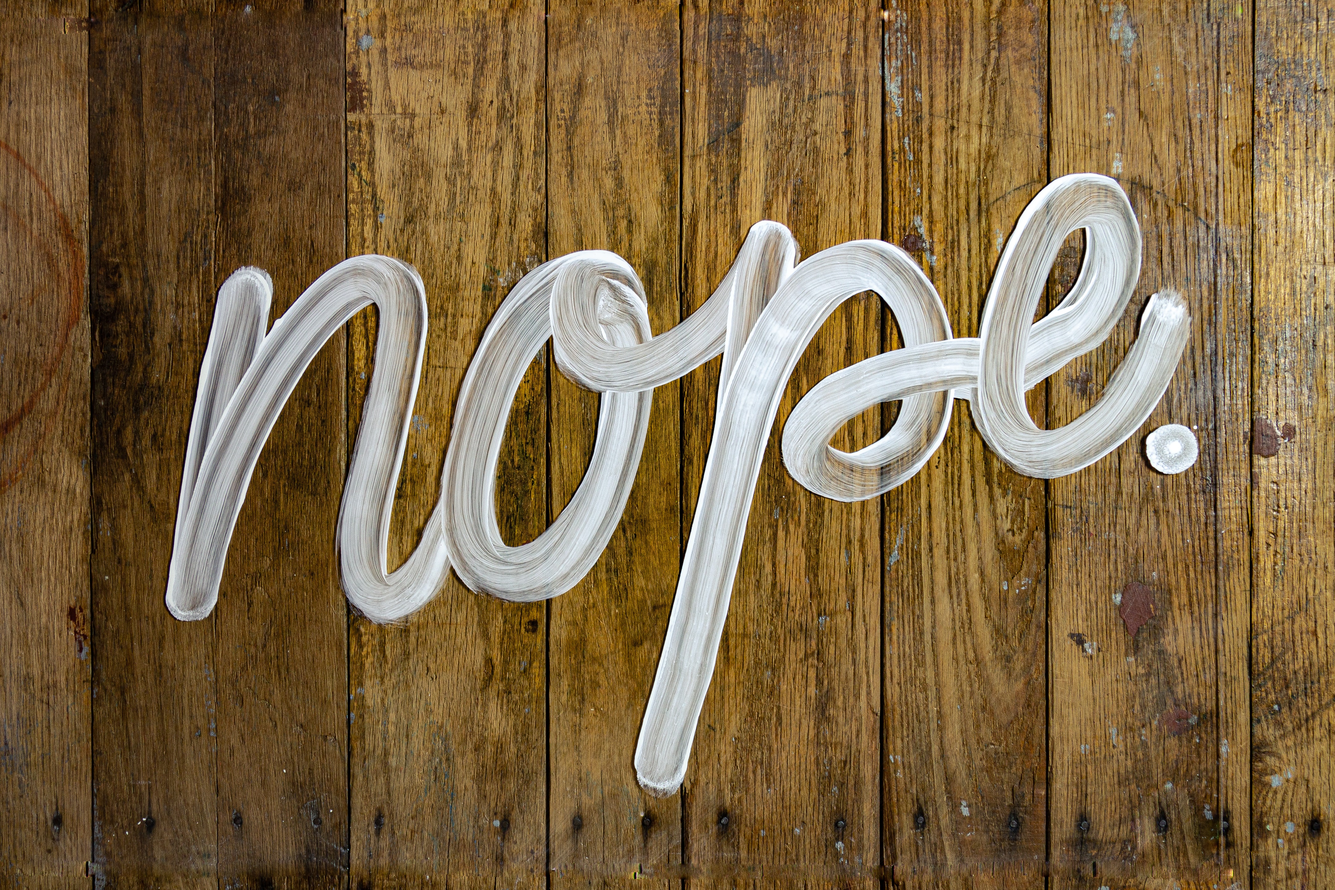 "Nope" written in white on a brown wood wall.