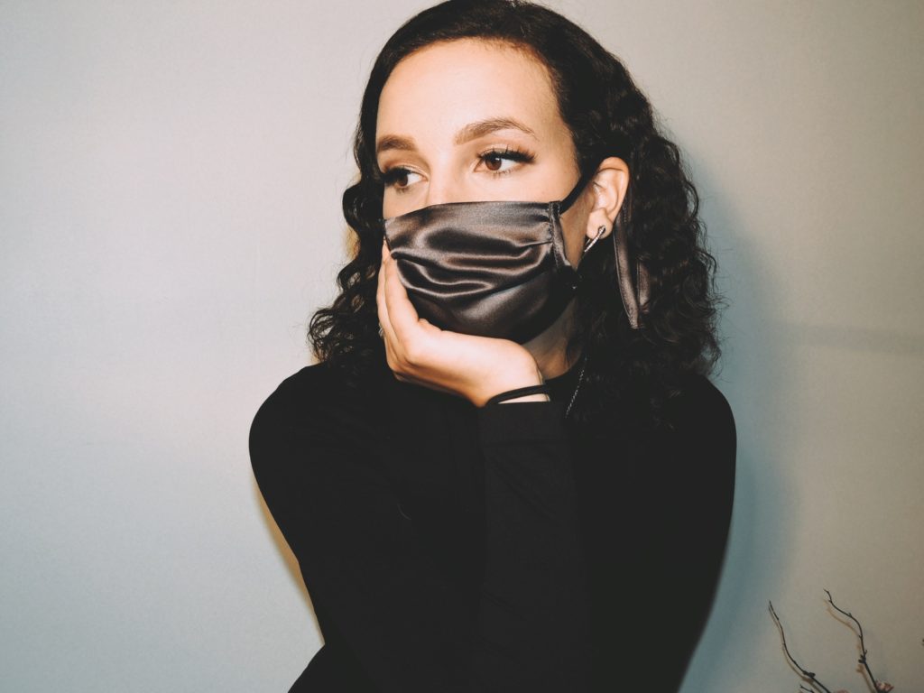 Tess Morgan wearing a black silk mask against a grey background.