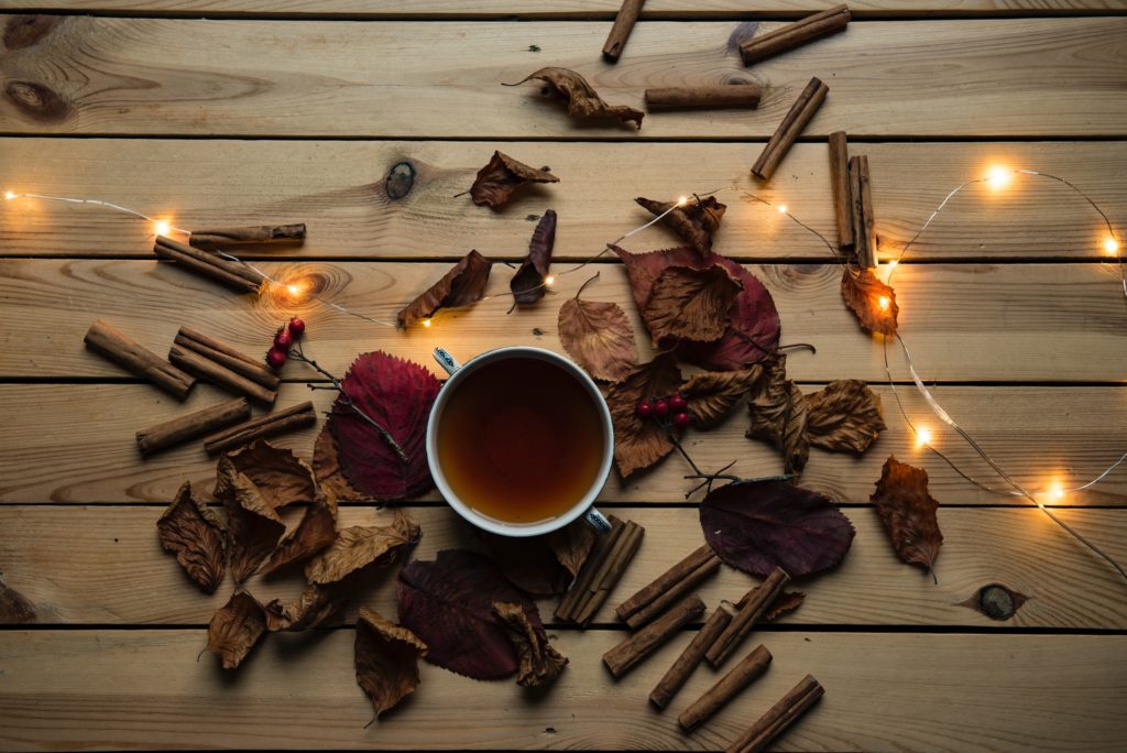 Cup of tea with cinnamon sticks, leaves, and fairy lights scattered on a table