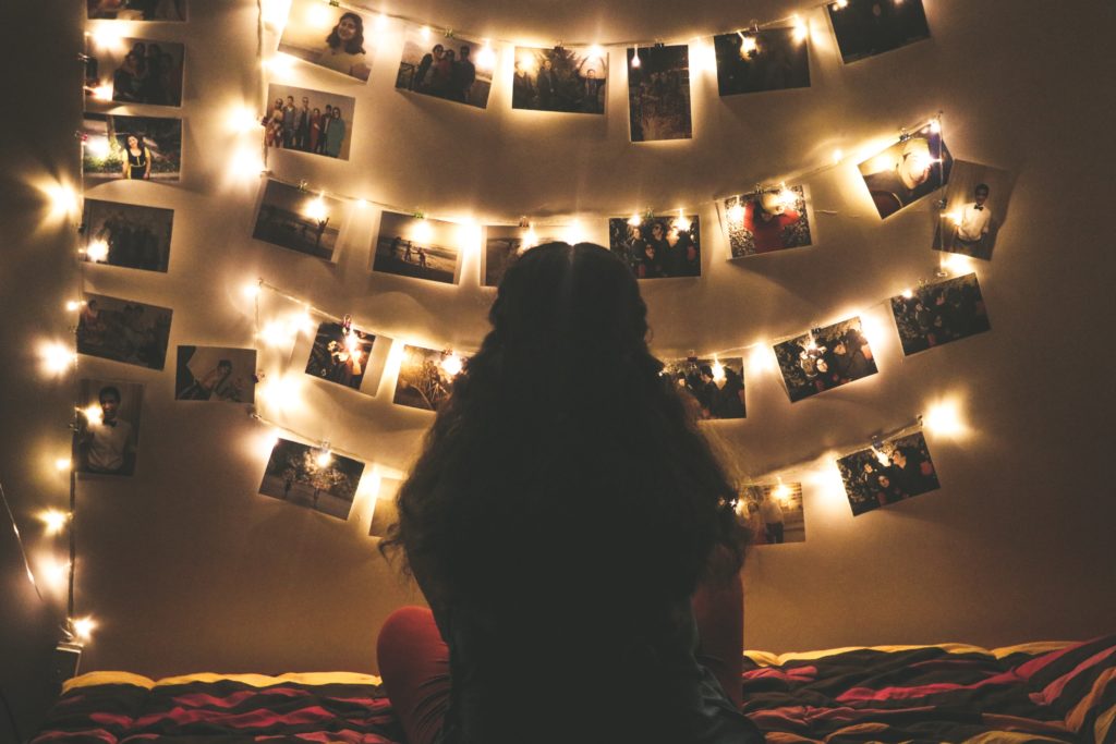 Silhouette of a person looking at fairy lights and photos on a wall.