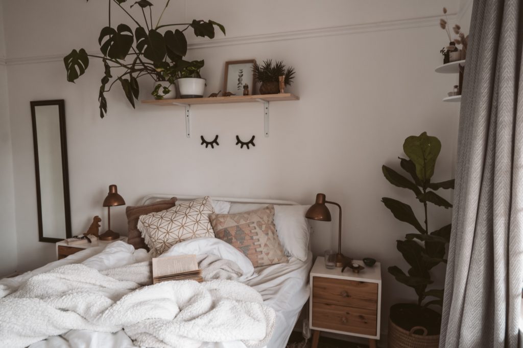 cozy bed with pillows and blankets. Plants and décor items around